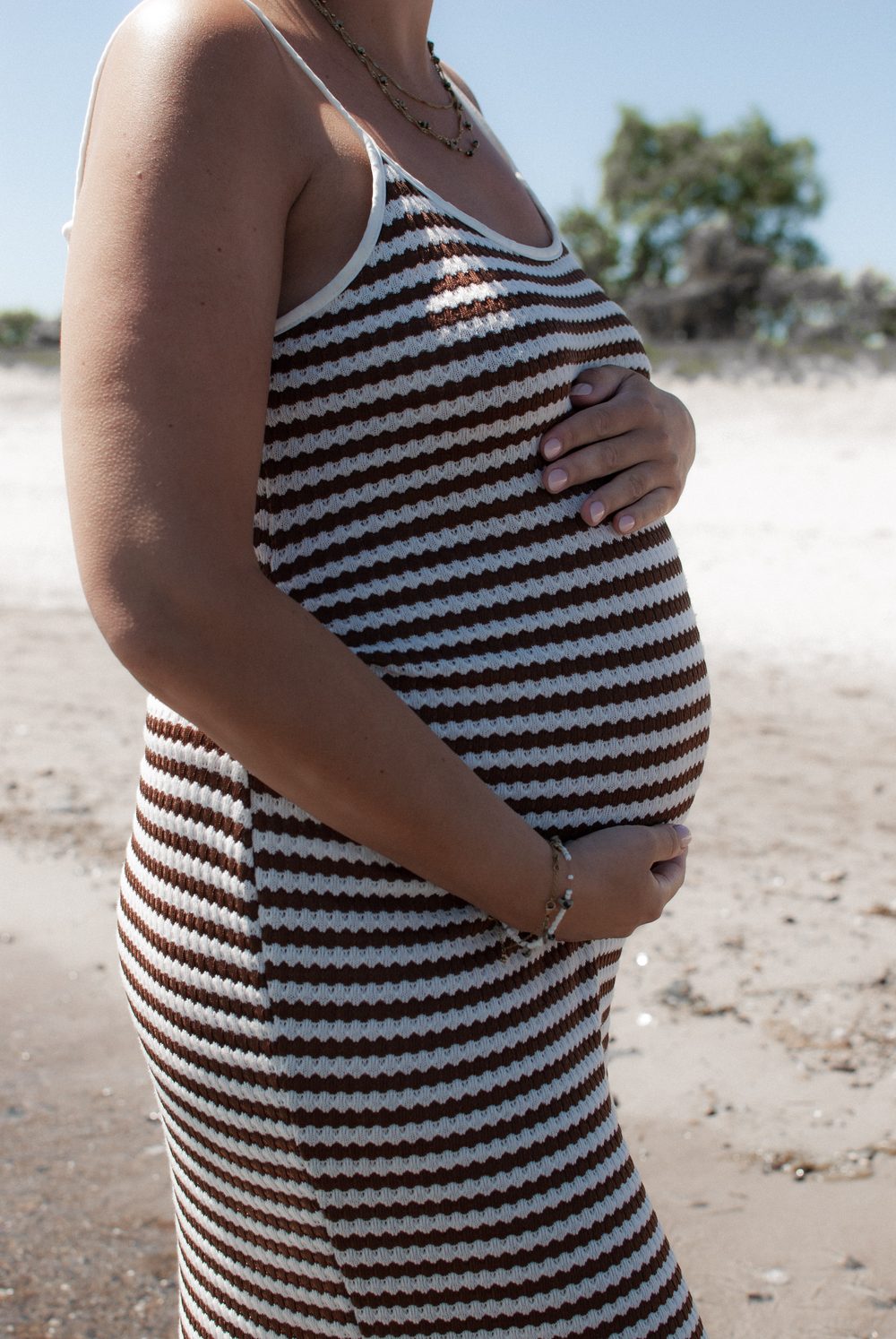 Nahaufnahme des Babybauchs im gestreiften Kleid, beide Hände liegen darauf